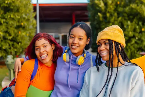 Three smiling teenage girls with arms around each other outdoors
