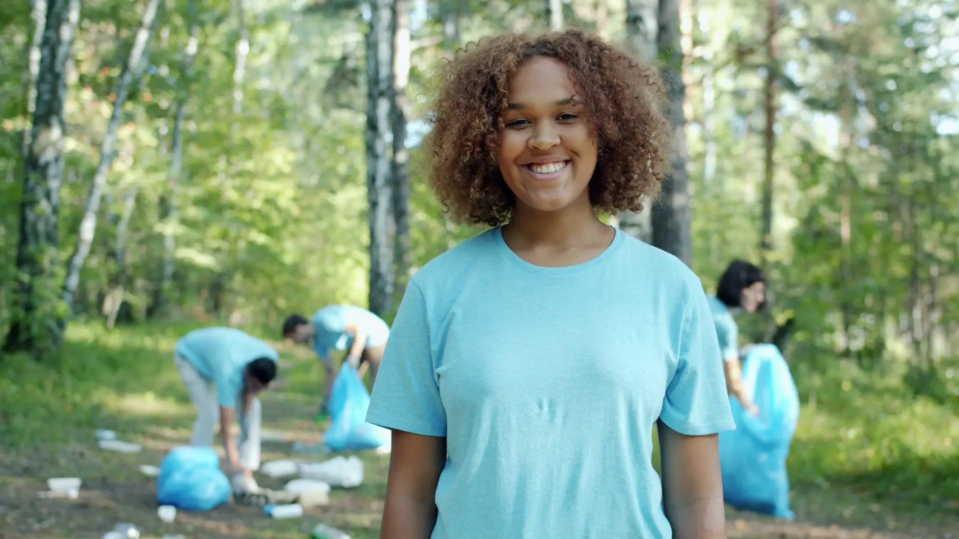 A smiling teenager volunteering at an outdoor community cleanup